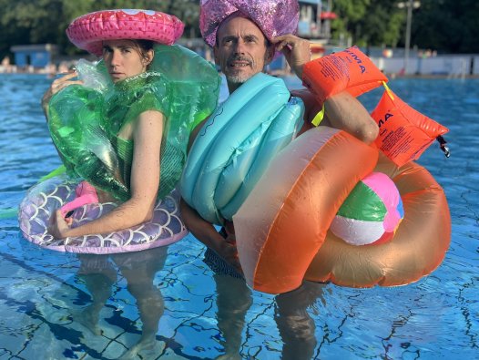 FELD Zentrale für junge Performance: BADESCHLUSS - Über den Sprung ins kalte Wasser | © Sabine Hilscher Zwei Personen stehen im Nichtschwimmerbecken, sie sind von oben bis unten behängt mit aufblasbaren Schwimmhilfen wie Schwimmflügel und Schwimmreifen. | © Sabine Hilscher