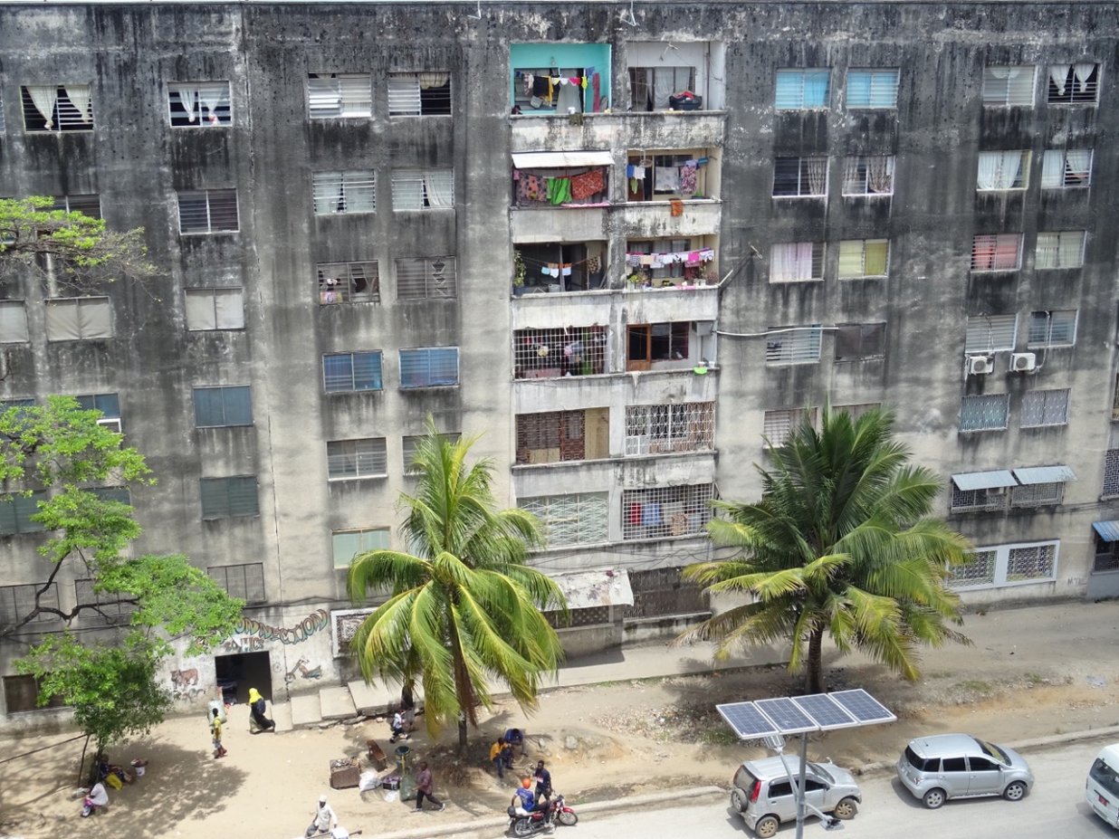 Die Fassade eines Plattenbaus in Sansibsar und ein Ausschnitt der davorliegenden Stra&szlig;e mit Autos und Palmen | © Sarah-Marleen Methner